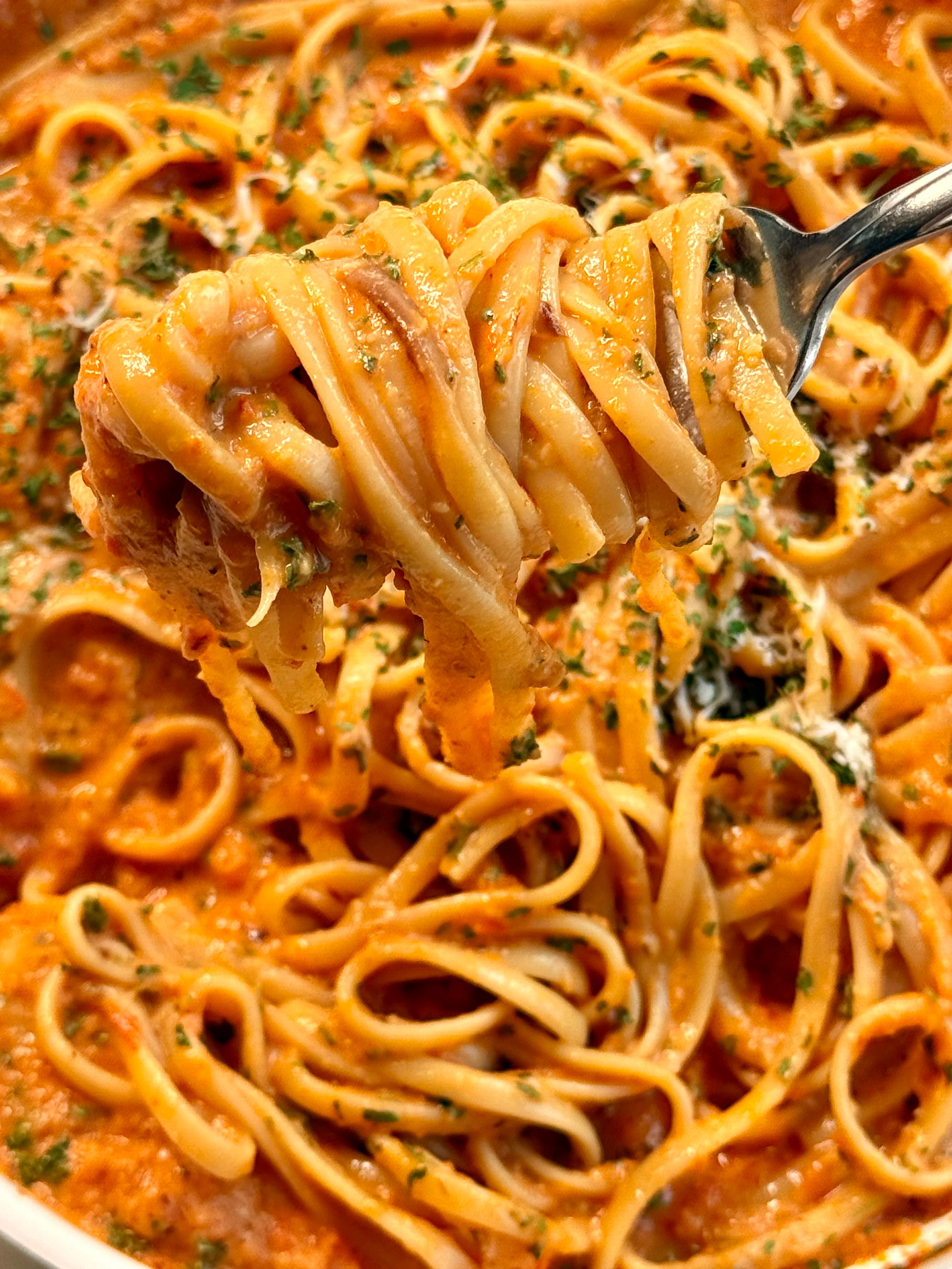 a white pan of creamy red pepper pasta with a metal fork