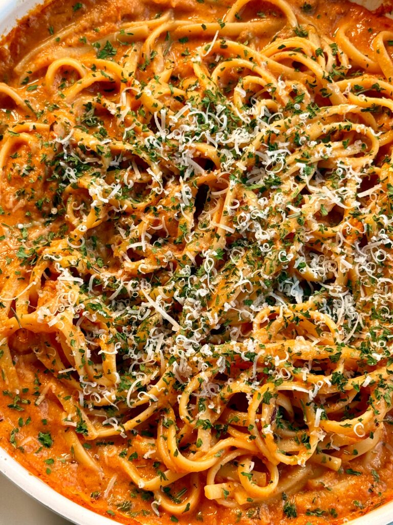 Detailed close-up of creamy red pepper pasta, highlighting the linguine noodles covered in a velvety roasted red pepper sauce, finished with a hearty sprinkle of parmesan cheese and fresh parsley for extra flavor and color.