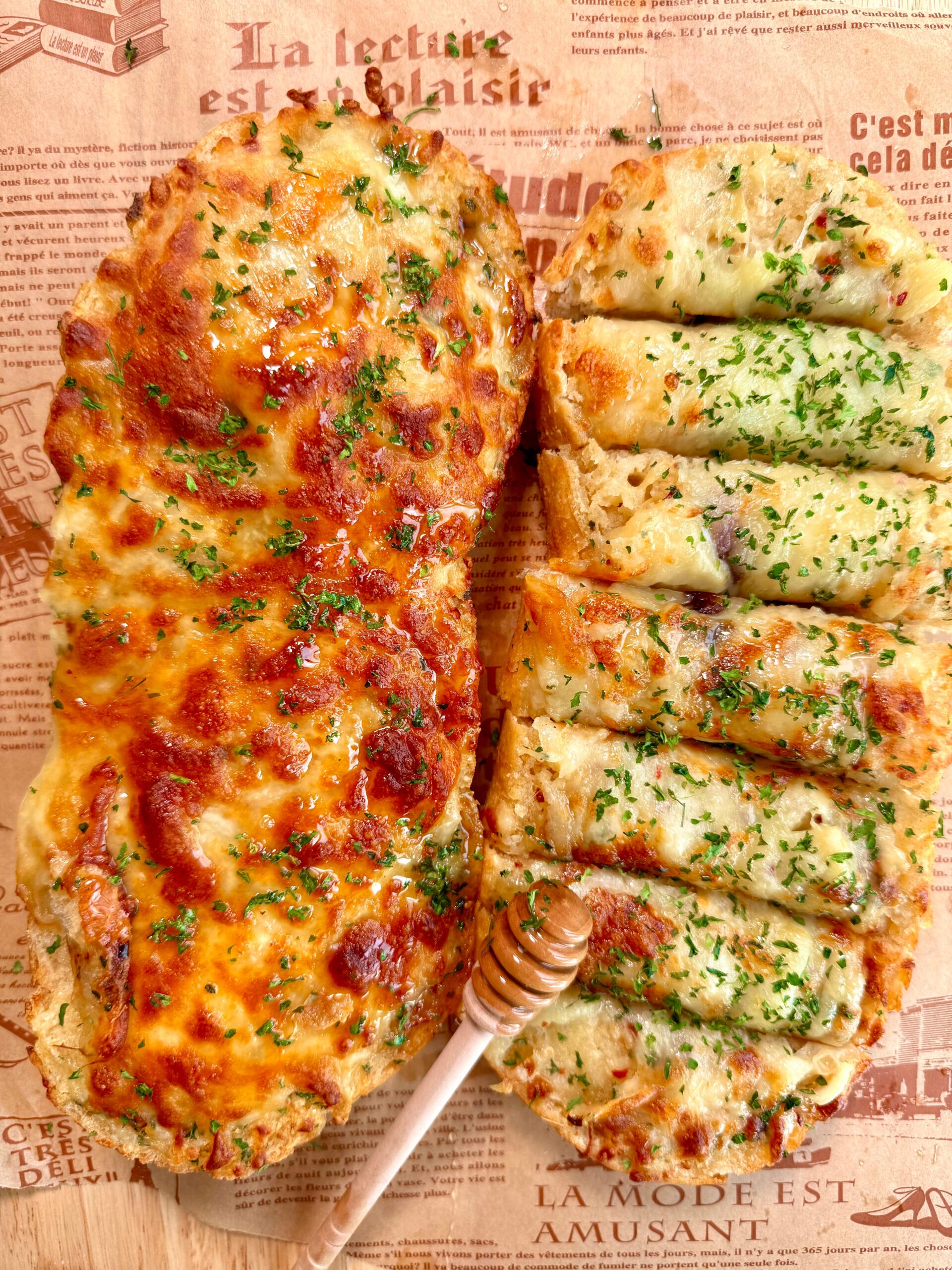 Close-up of honey garlic bread with melted mozzarella, golden edges, and a honey dipper on the side