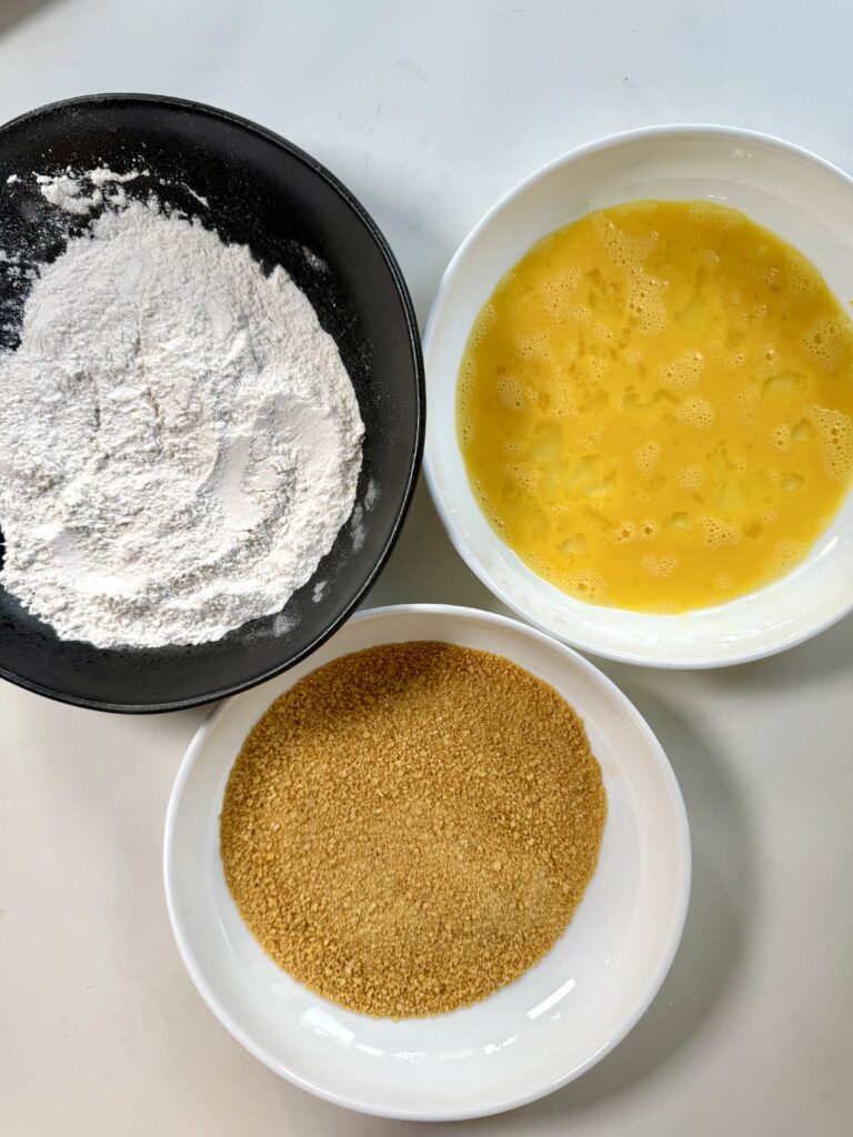 Three bowls for breading chicken patties: flour, beaten egg, and corn flakes crumbs